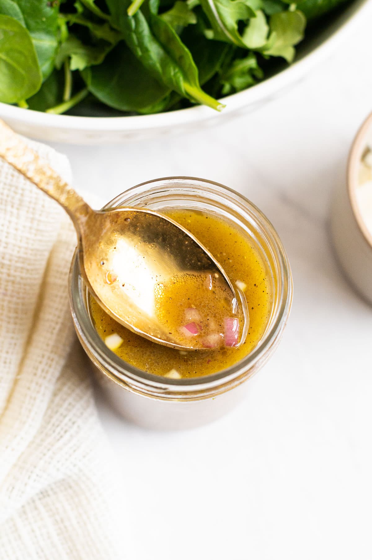 Close up of spinach salad dressing with red onion on a spoon.