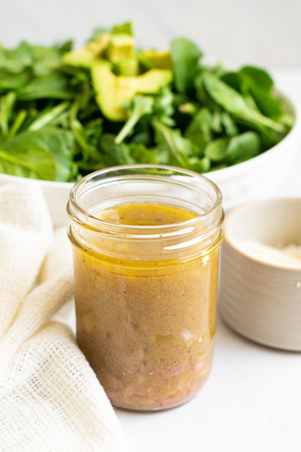 Spinach salad dressing in a jar with salad in a bowl behind it.
