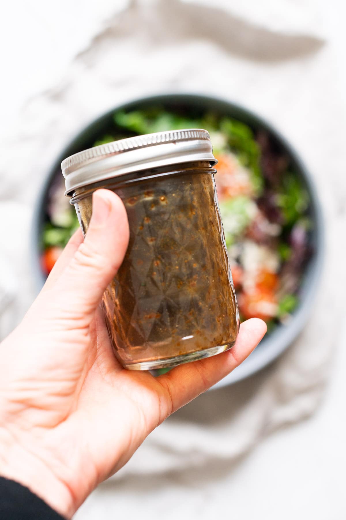 Person holding a jar with balsamic dressing over a bowl of salad.