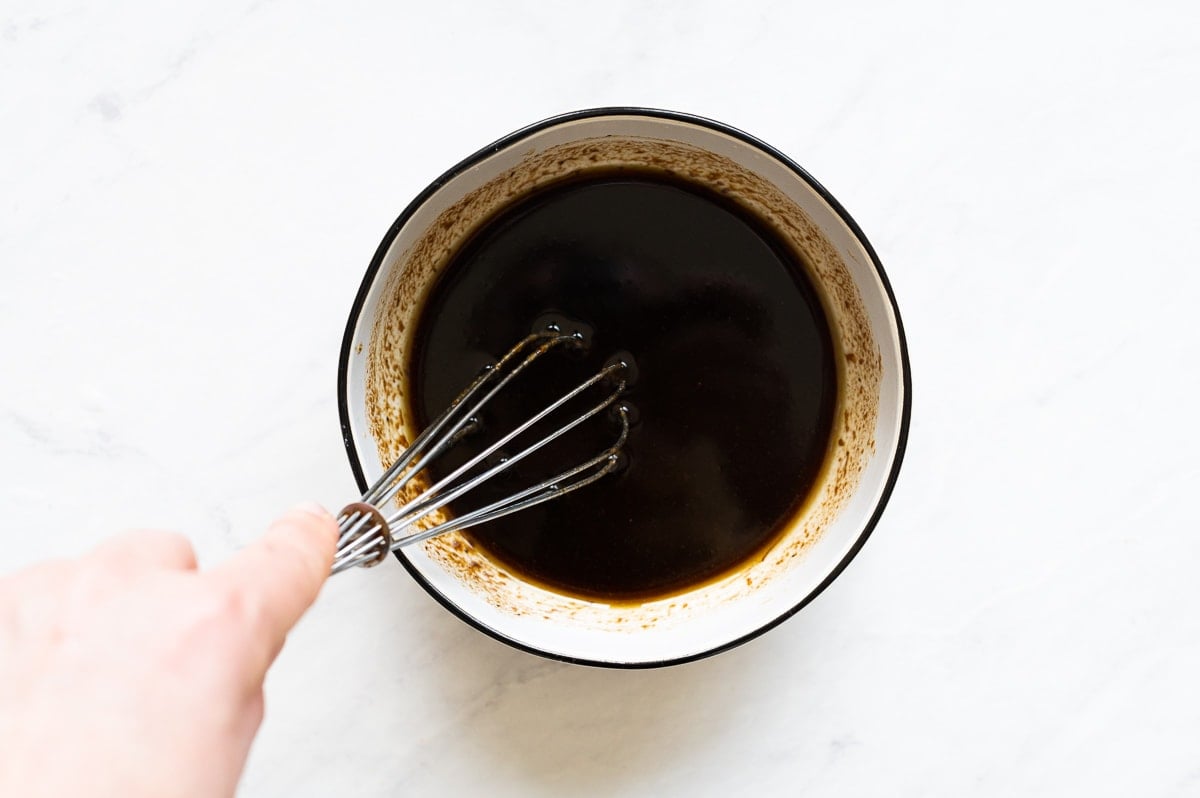 Person whisking balsamic vinaigrette in white bowl.