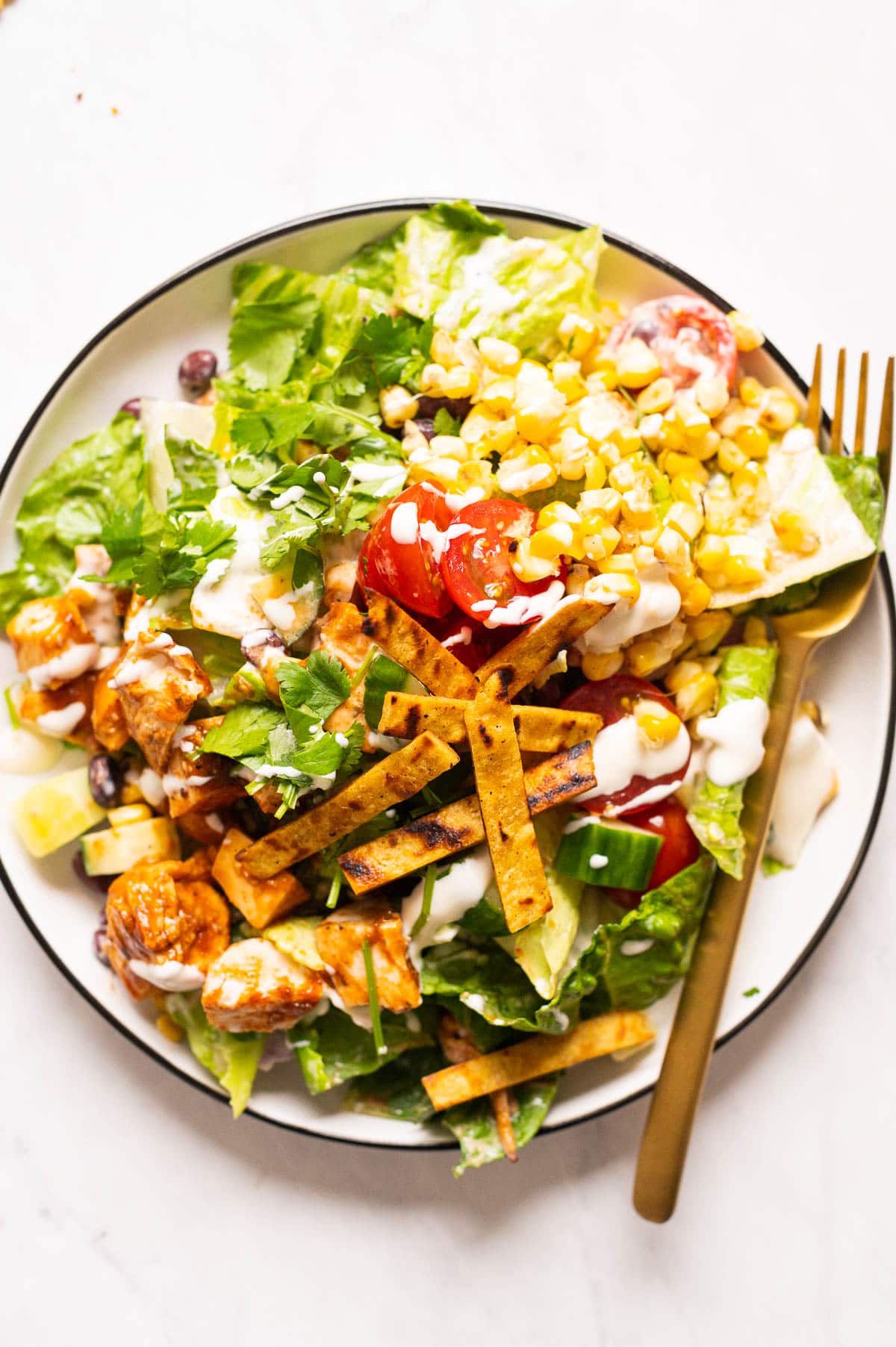 Barbecue chicken salad with corn, tomatoes, barbecue chicken and tortilla strips served on a plate.