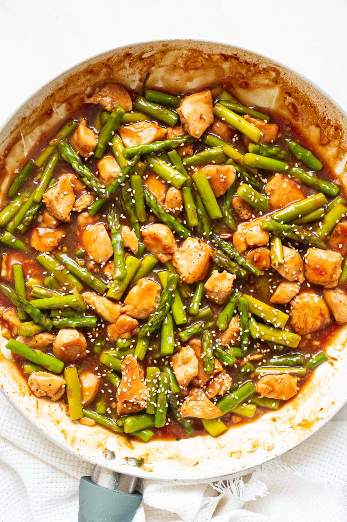 Chicken asparagus stir fry garnished with sesame seeds in a skillet.