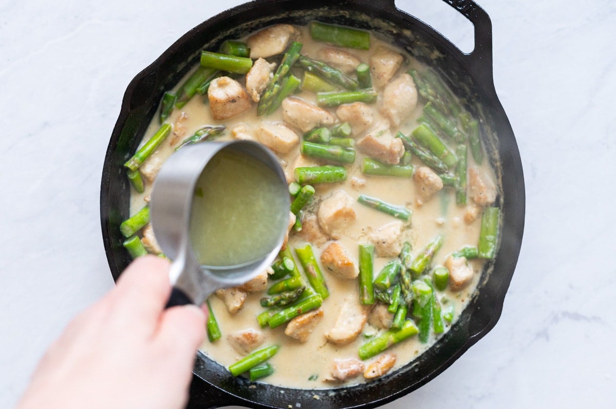 Person pouring lemon juice over chicken and asparagus recipe.