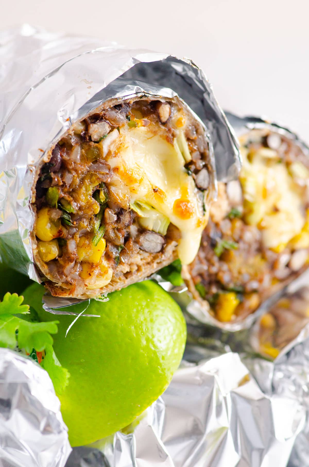 Chicken burritos wrapped in aluminum foil showing texture inside with melted cheese.
