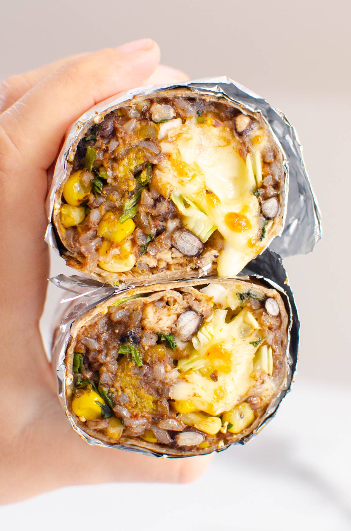 Person holding two chicken burritos showing texture inside.