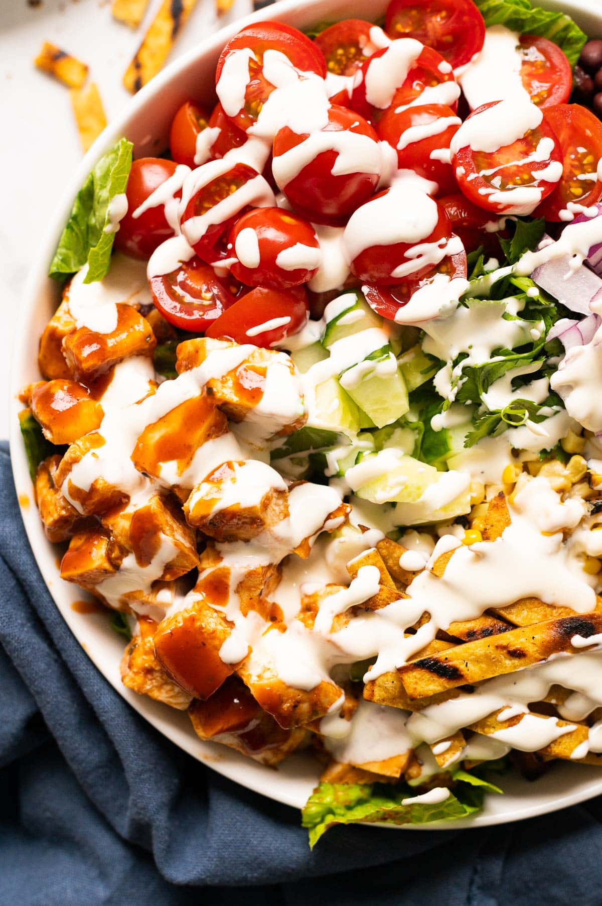 Close up of BBQ chicken salad drizzled with ranch dressing in white bowl.