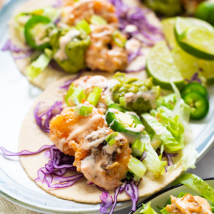 Bang bang shrimp tacos with lettuce, red cabbage, jalapeno and sauce served on a plate.