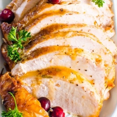 Instant Pot turkey breast with gravy, parsley and cranberries on a platter.