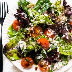 Spring mix salad with cherry tomatoes and parmesan cheese on white plate.