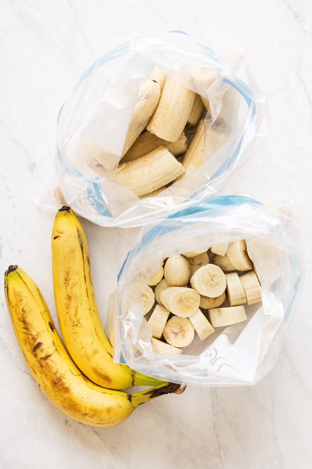 Sliced and half frozen bananas in resealable bags. Two ripe bananas.