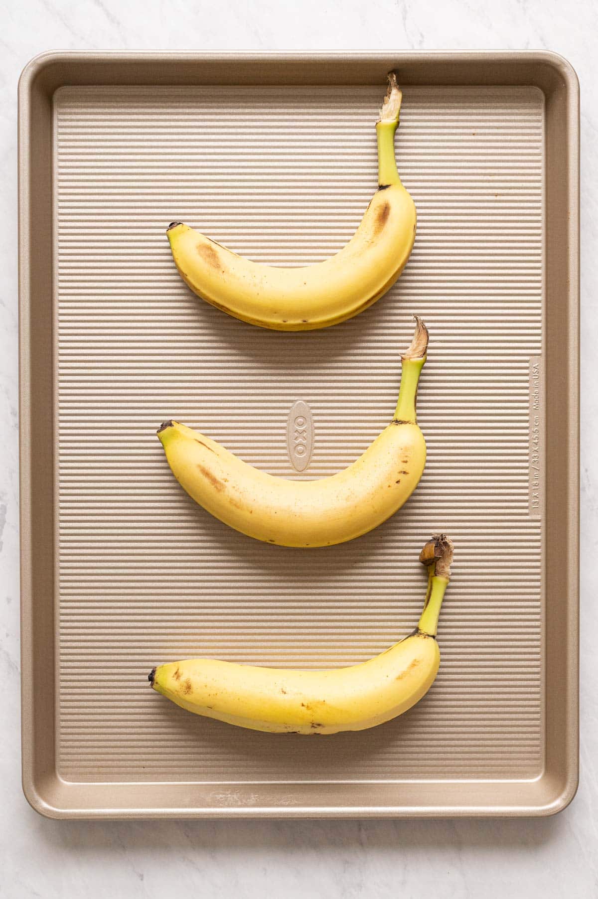 Three yellow bananas on a baking sheet.