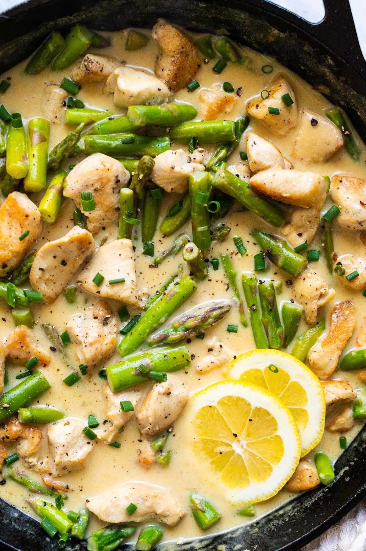 Close up of chicken and asparagus recipe in creamy sauce with lemon slices.
