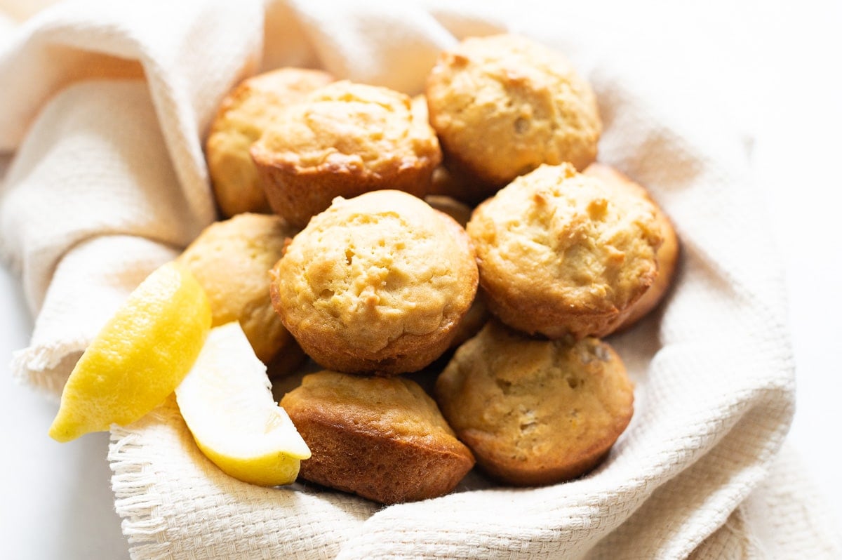 Lemon muffins served in a dish lined with linen towel and a few lemon slices.