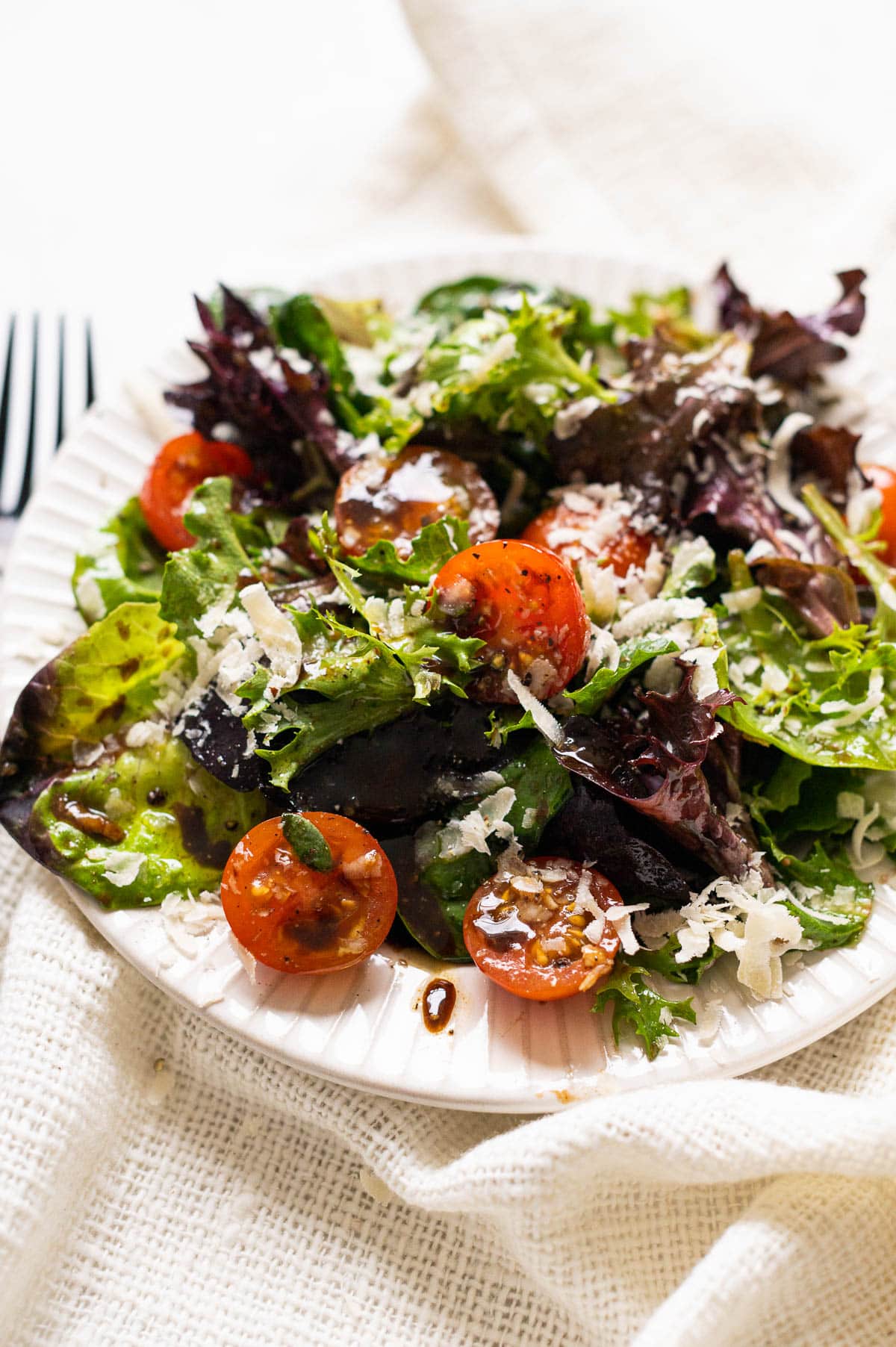 Spring mix salad with cherry tomatoes and parmesan cheese on white plate.
