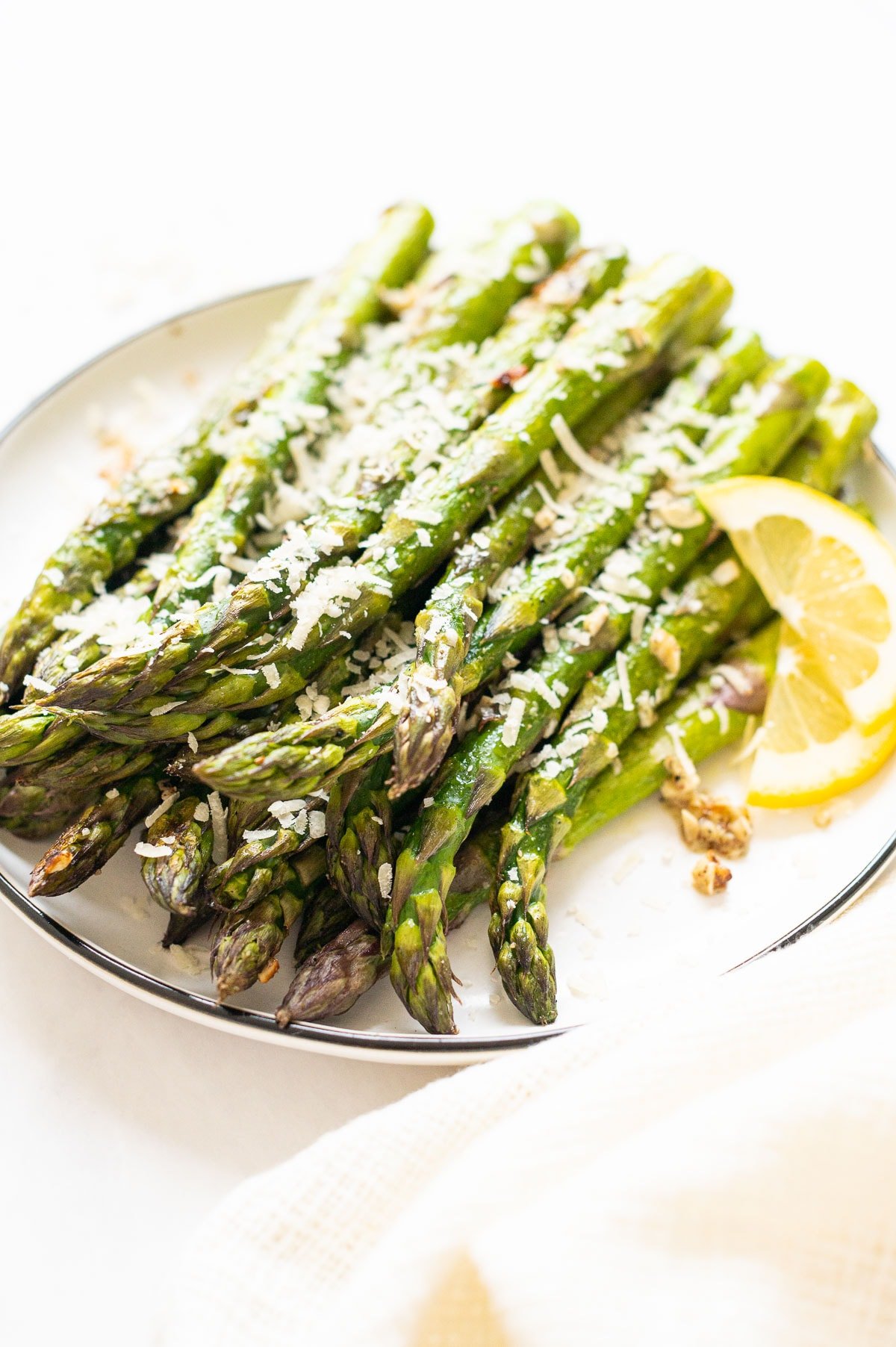 Oven roasted asparagus recipe served on a plate with Parmesan and lemon slices.