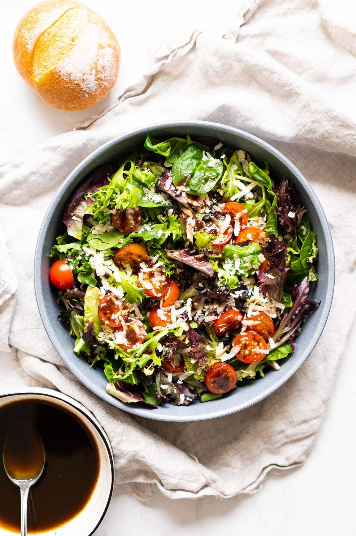 Simple spring mix salad served in a bowl with a bowl of balsamic  and a bun on a side.