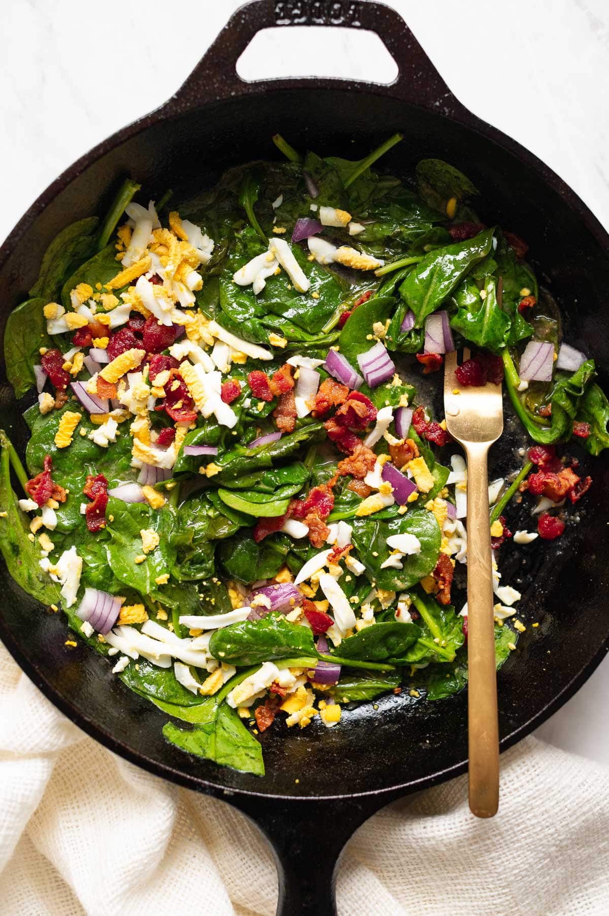 Wilted spinach salad recipe with grated hard boiled eggs, bacon bits and chopped red onion.