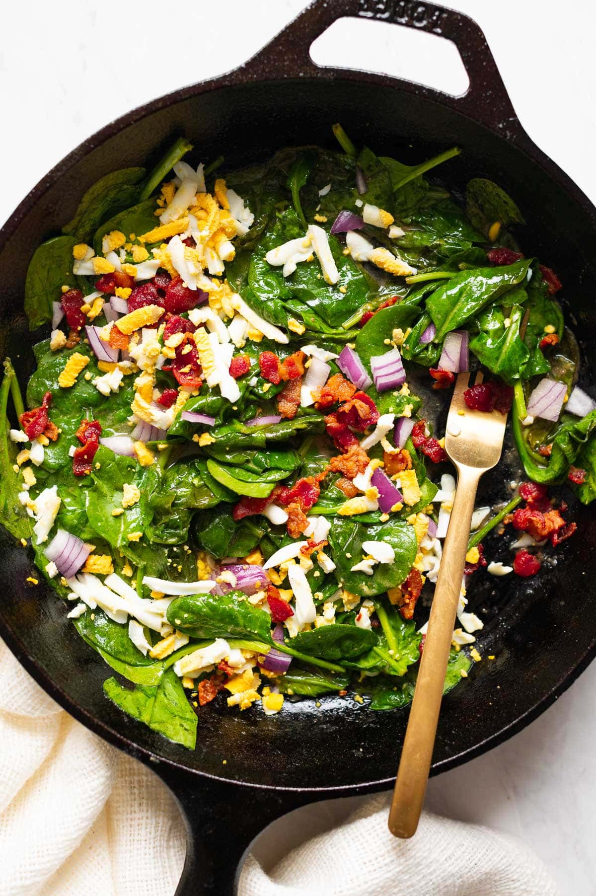 Wilted spinach salad served in a cast iron skillet with a fork.
