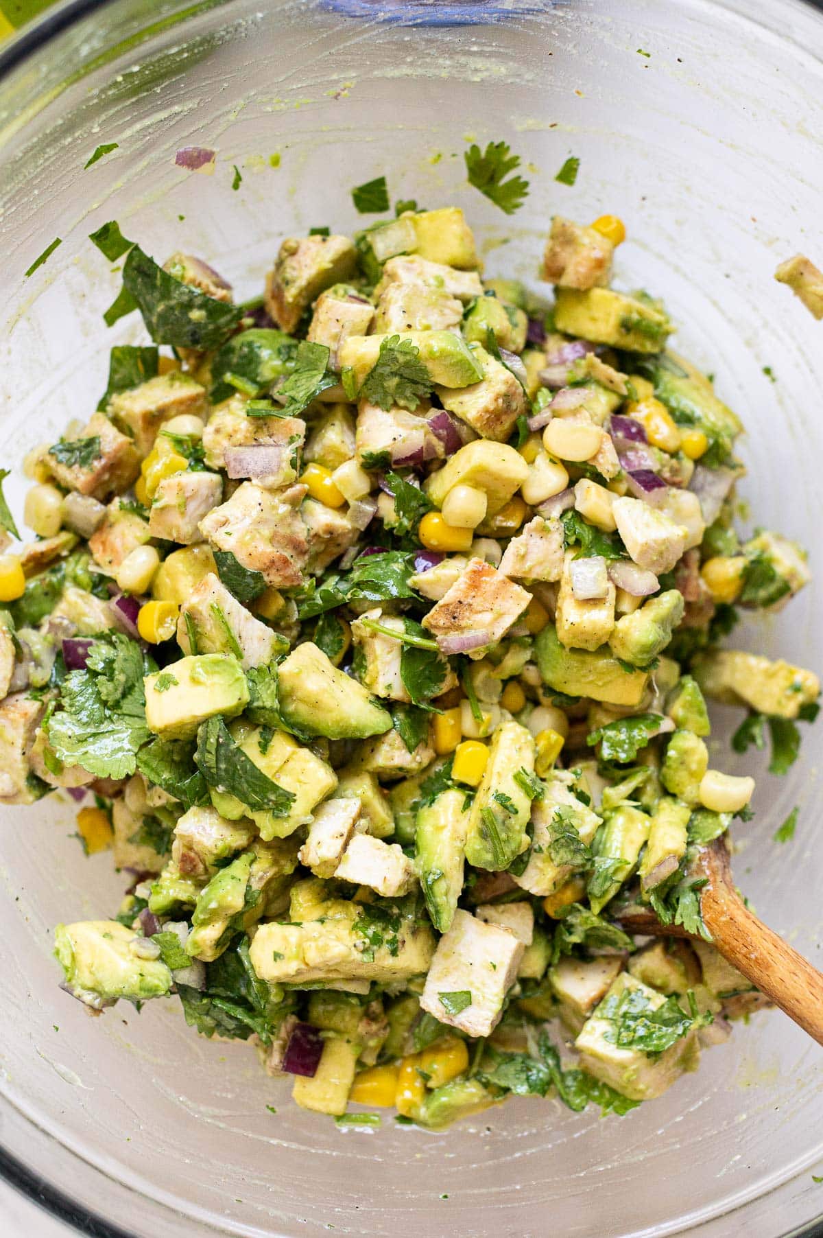 Avocado chicken salad in a glass bowl with wooden spoon.