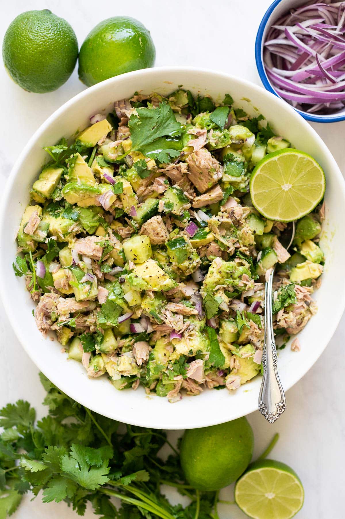Avocado tuna salad with lime and cilantro served in a bowl with metal spoon.