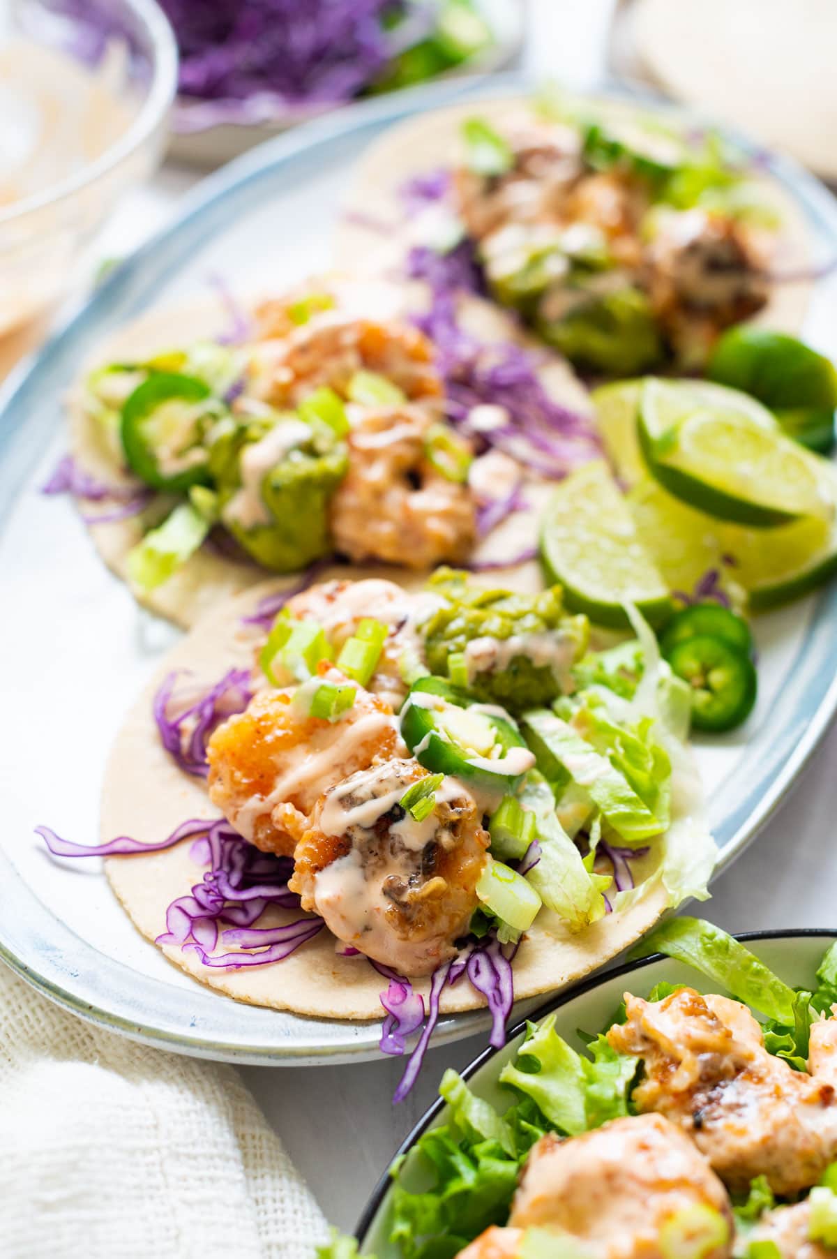 Bang bang shrimp tacos with lettuce, red cabbage, jalapeno and sauce served on a plate.