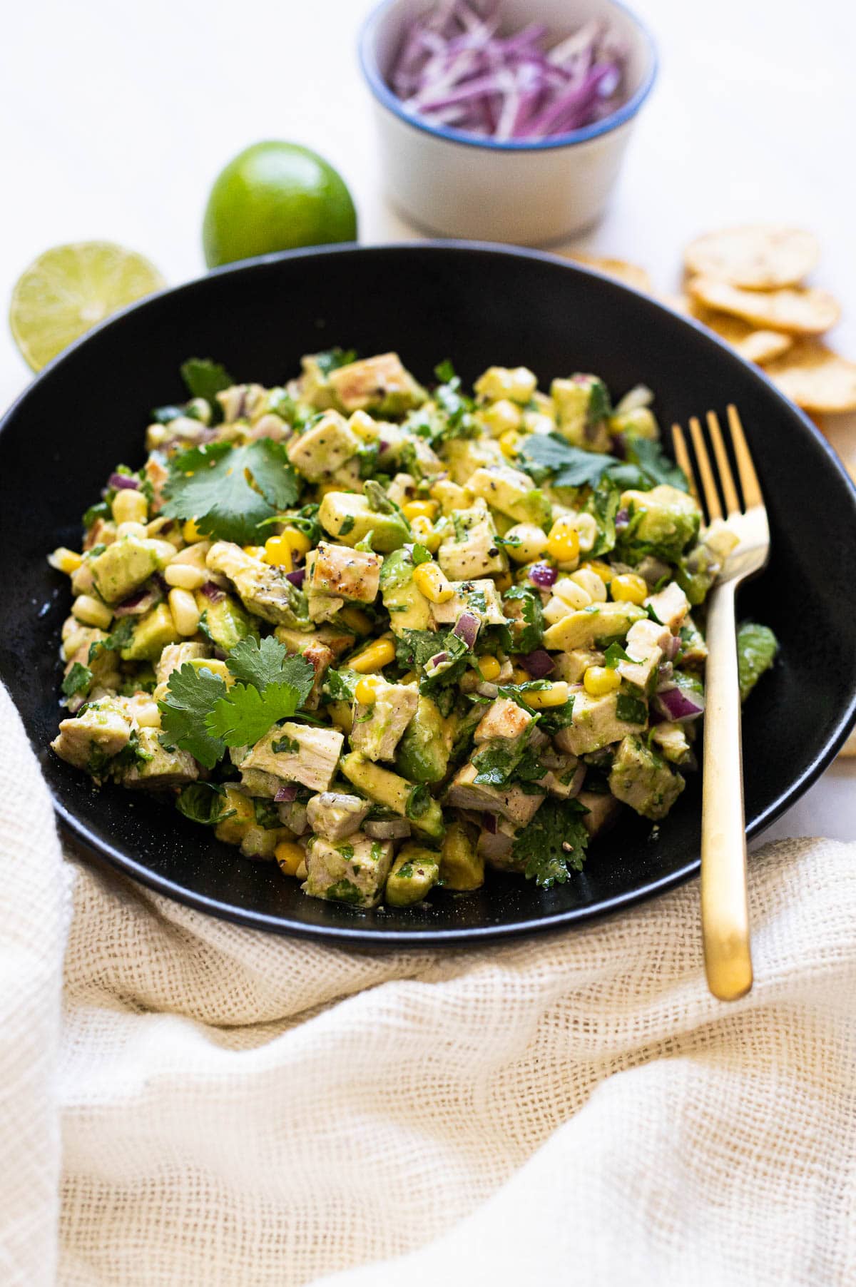 Chicken avocado salad in black bowl with golden fork.