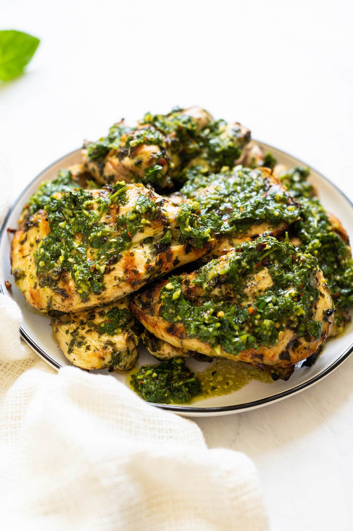 Side view off grilled chicken chimichurri breasts topped with chimichurri sauce.