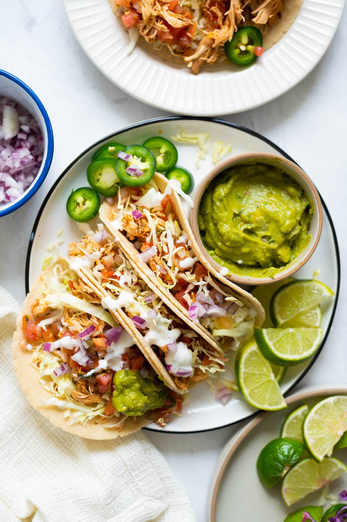 Instant Pot chicken tacos served with guacamole, lime and jalapenos on a plate.