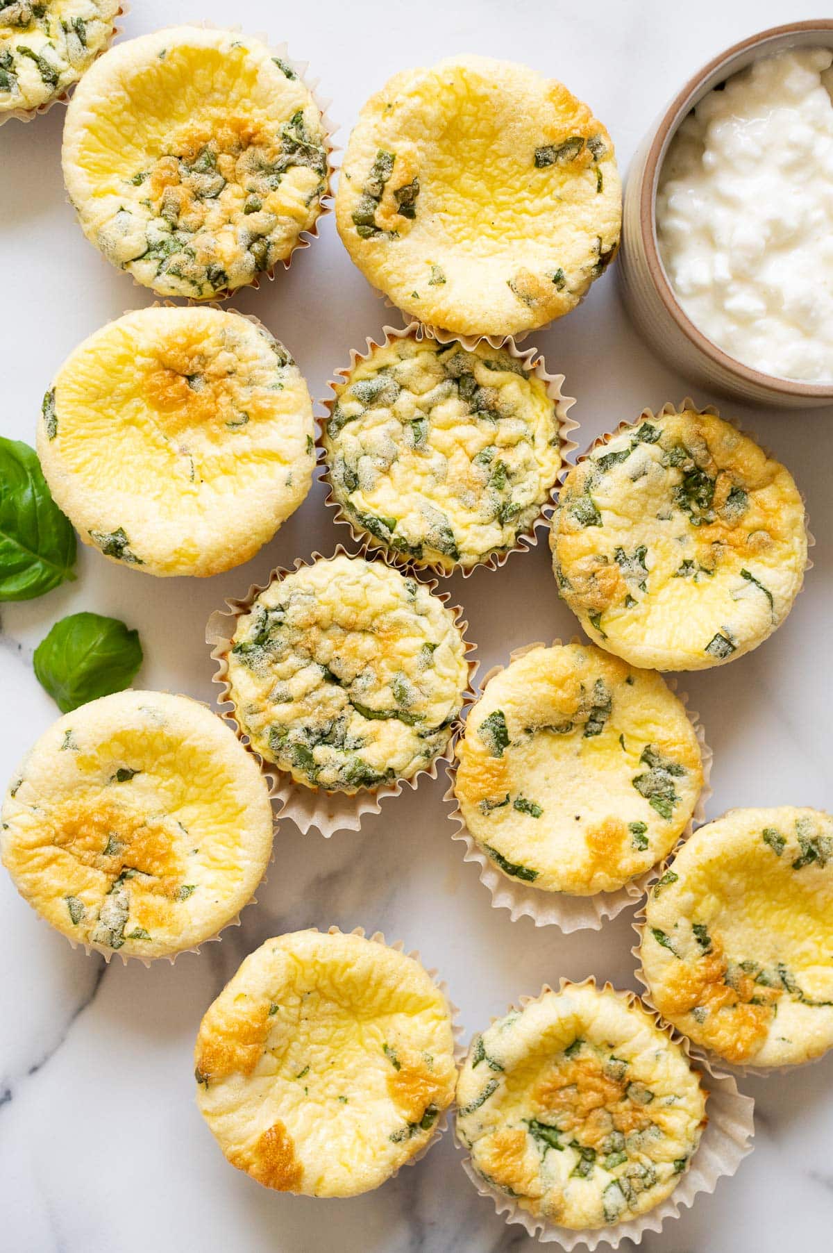 Cottage cheese egg bites on a countertop and fresh basil leaves and a bowl with cottage cheese.
