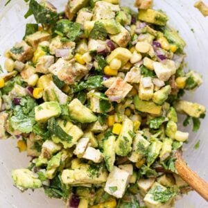 Avocado chicken salad in a glass bowl with wooden spoon.