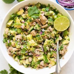 Avocado tuna salad with lime and cilantro served in a bowl with metal spoon.