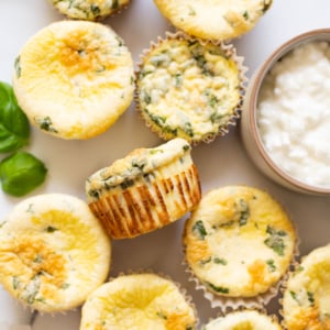 Cheese egg bites on a countertop and fresh basil leaves and a bowl with cottage cheese.