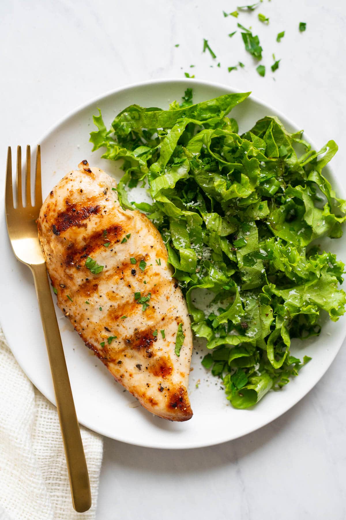 Grilled chicken breast served with lettuce salad on a plate with a fork.