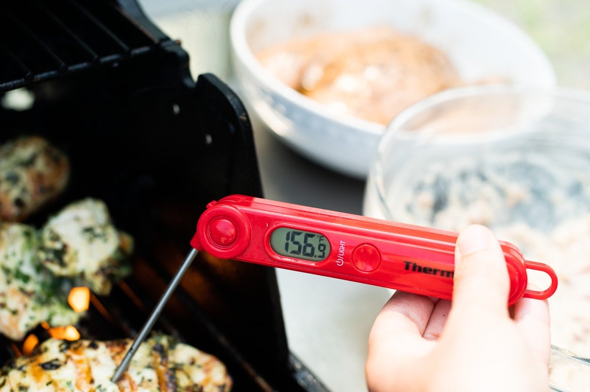 Person measuring cooked yogurt marinated chicken with an instant bread thermometer that reads 156 F.
