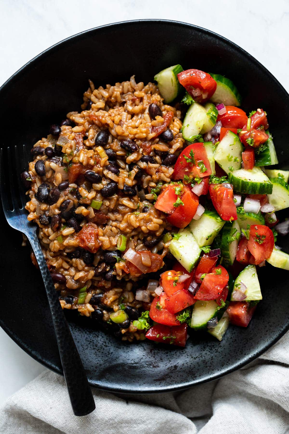 Instant Pot rice and beans with cucumber tomato salad on black plate with a fork.