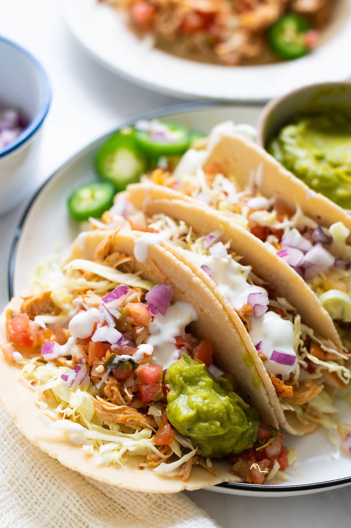 Instant Pot shredded chicken tacos with cabbage, pico de gallo, guacamole and crema served on a plate.