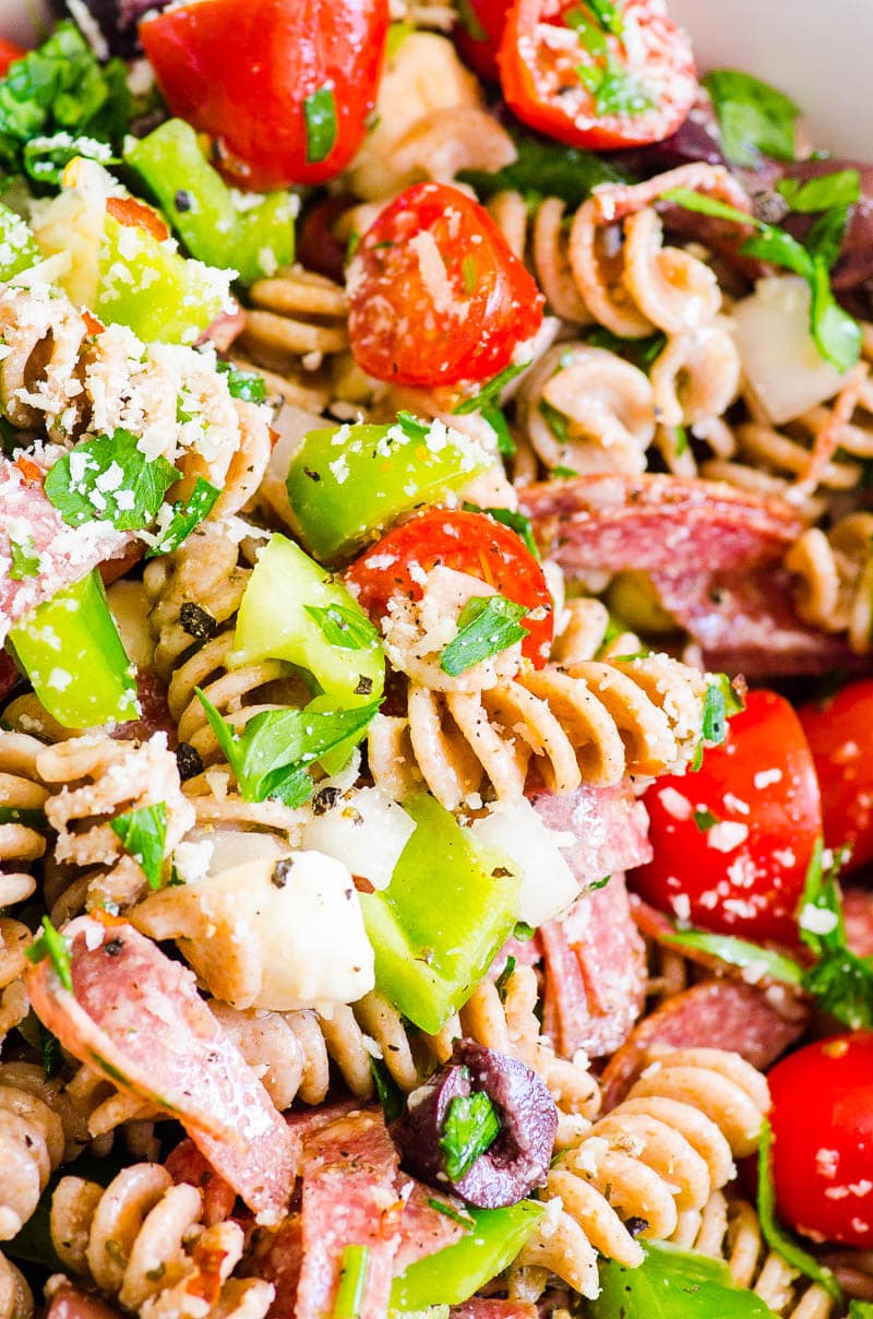 Close up of Italian pasta salad showing pasta, green bell pepper, grape tomatoes, salami, parsley and cheese.