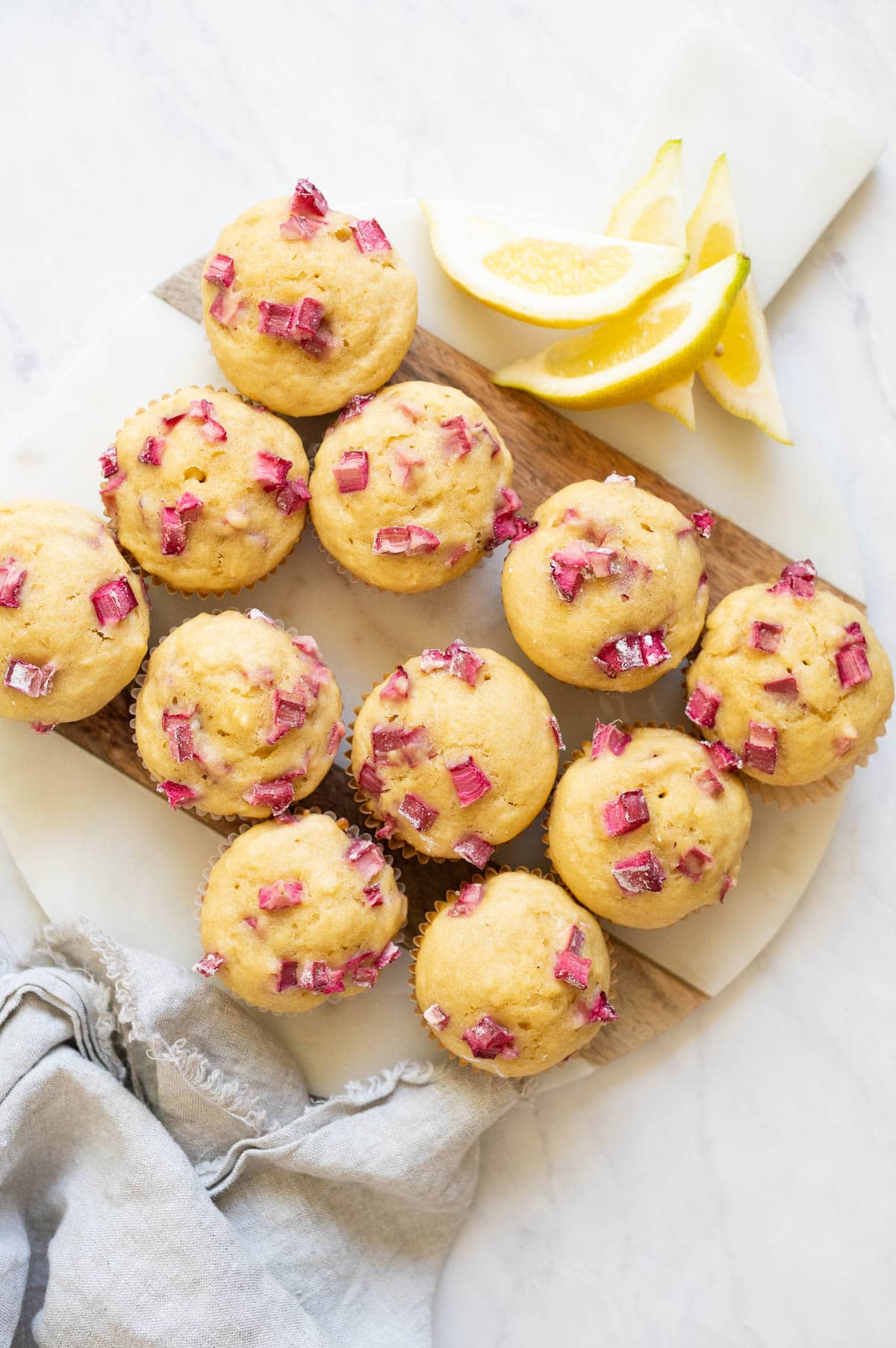 View from top on rhubarb muffins on a plate with lemon slices and napkin near it.