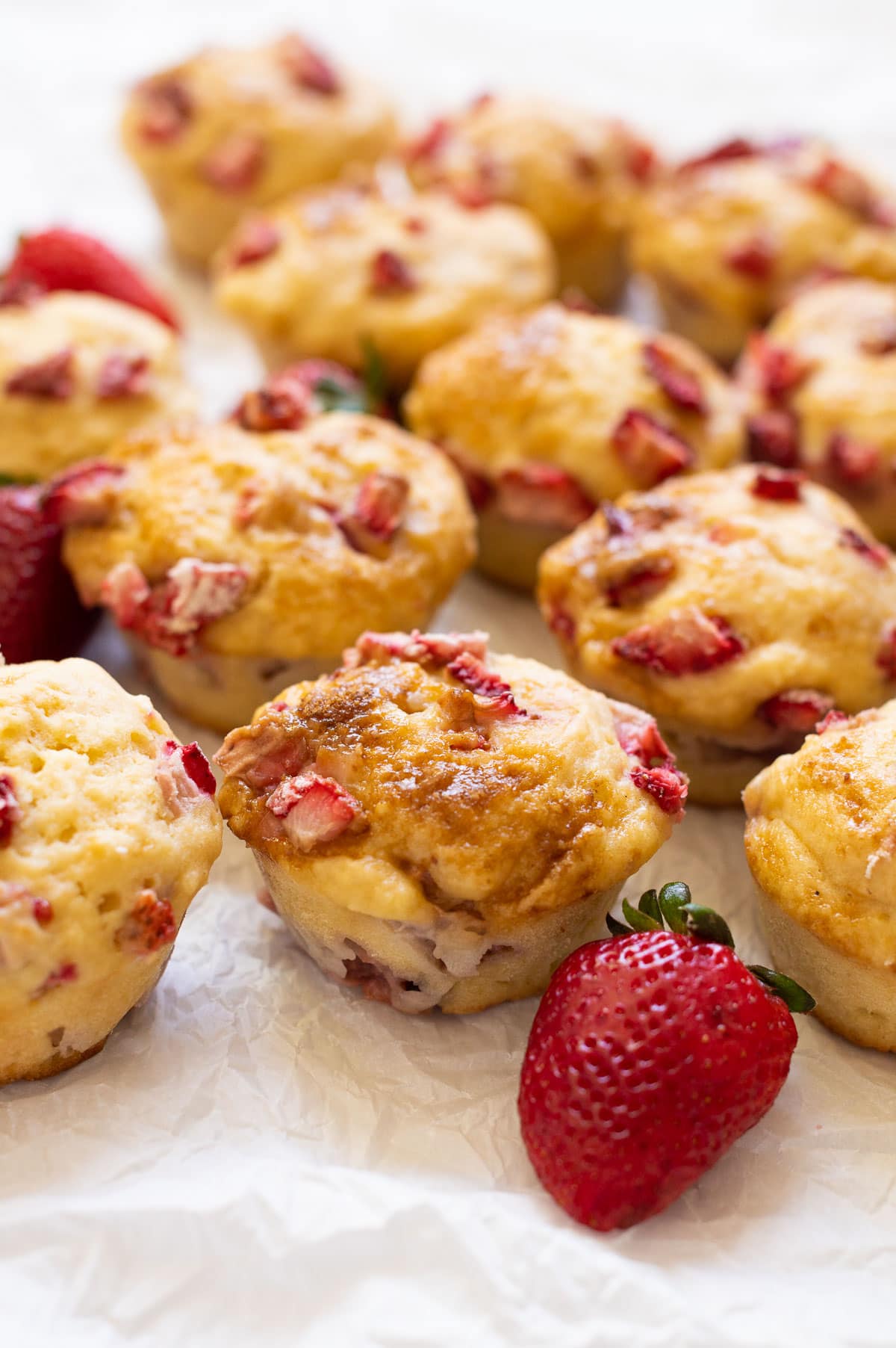 Strawberry muffins on parchment paper with fresh strawberries around them.