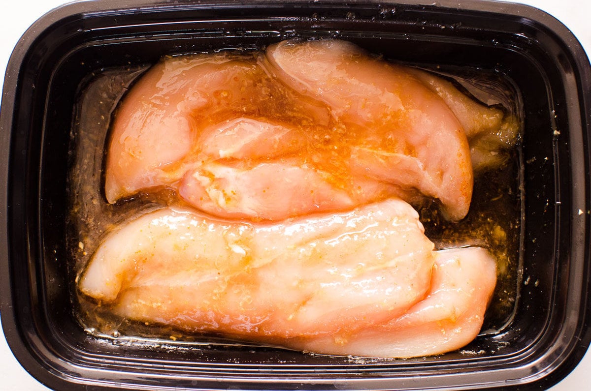 Chicken breasts in teriyaki chicken marinade in black container.