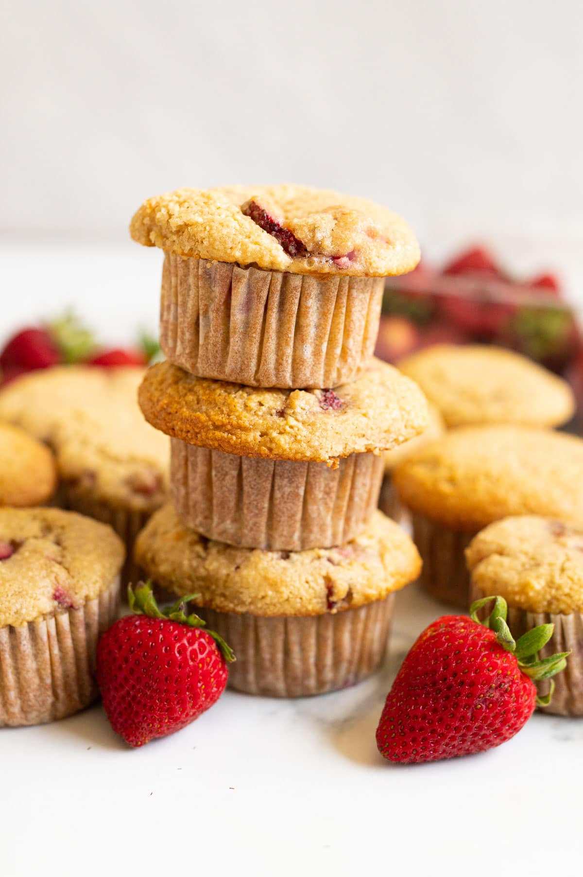 A stack of 3 almond flour strawberry muffins with strawberries and muffins around it.