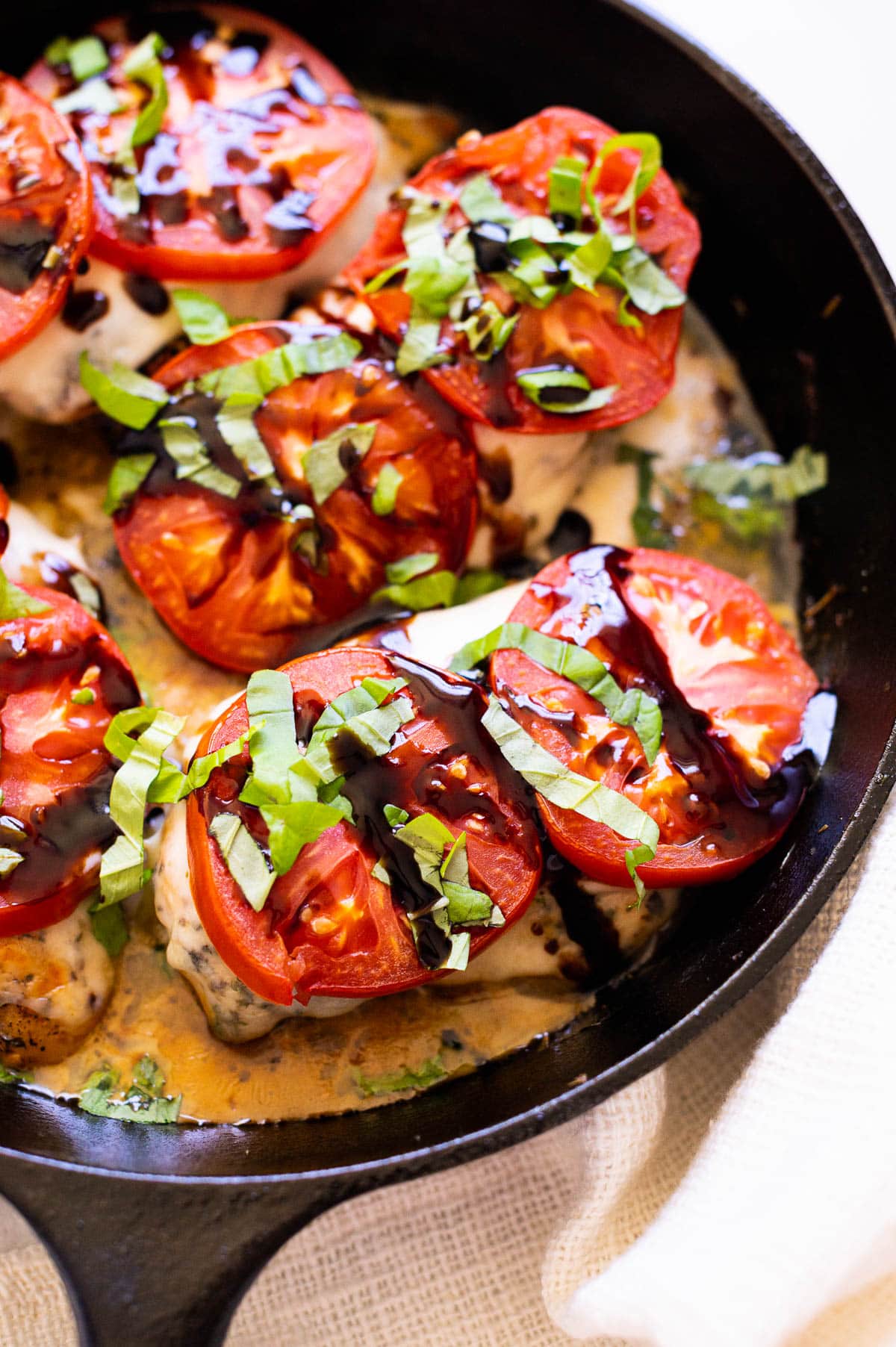 Chicken caprese topped with fresh basil and balsamic glaze and served in cast iron skillet.