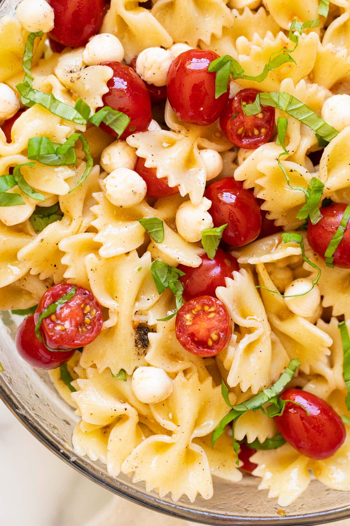 Close up of caprese pasta salad with grape tomatoes, cocktail bocconcini,  fresh basil and bow tie pasta.