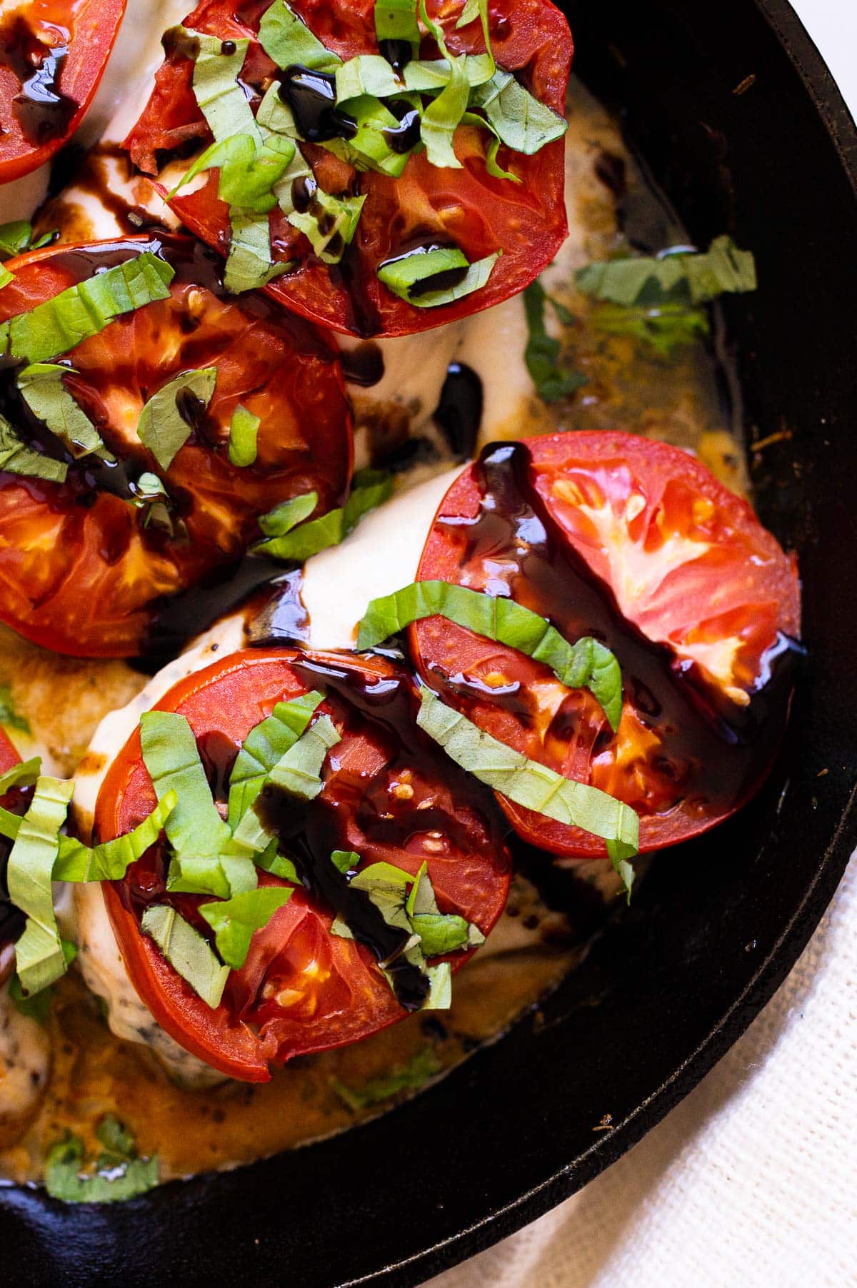 Baked chicken caprese garnished with balsamic glaze and fresh basil in a skillet.