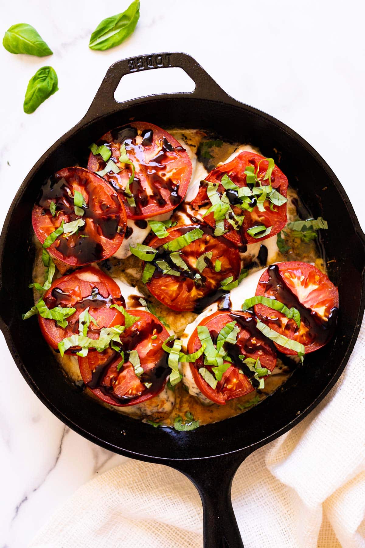 Four caprese chicken breasts with sauce in a cast iron skillet.