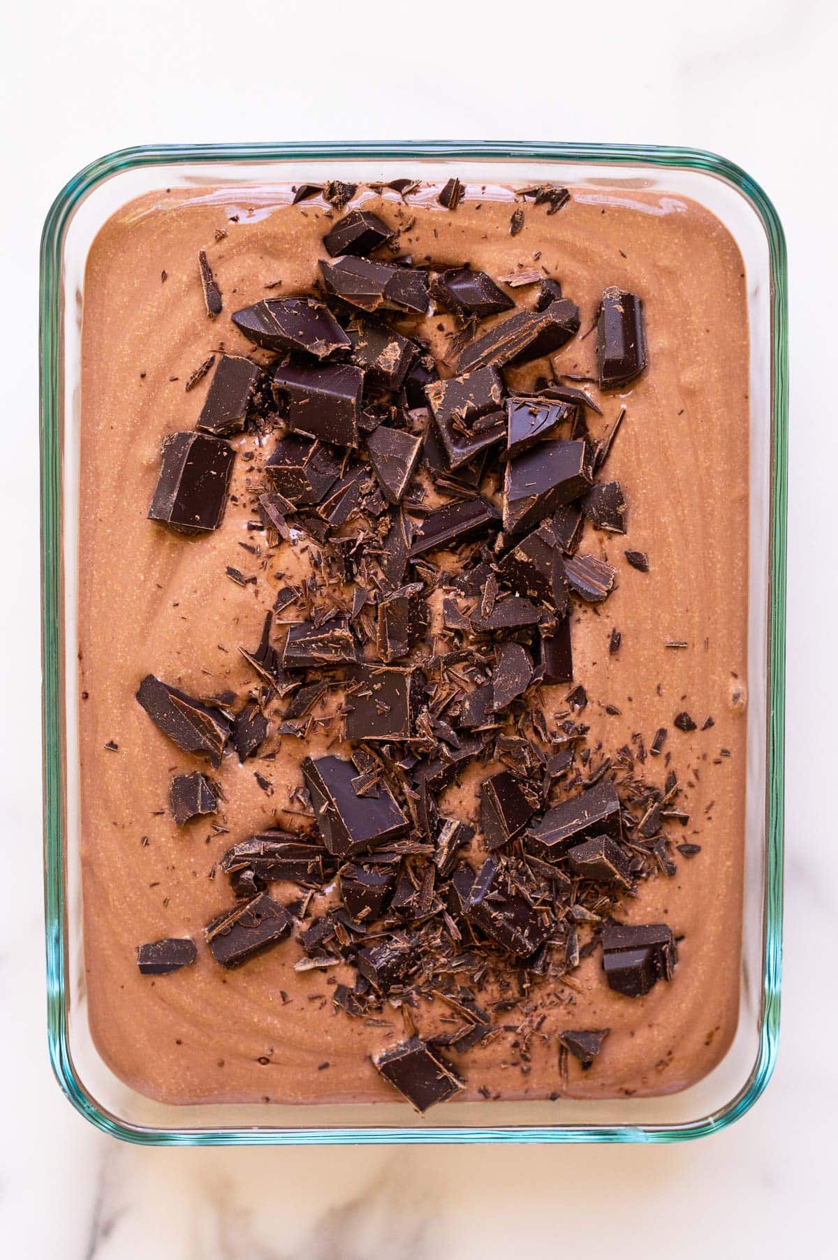 Chocolate cottage cheese ice cream topped with chopped chocolate bar in a glass container before freezing.