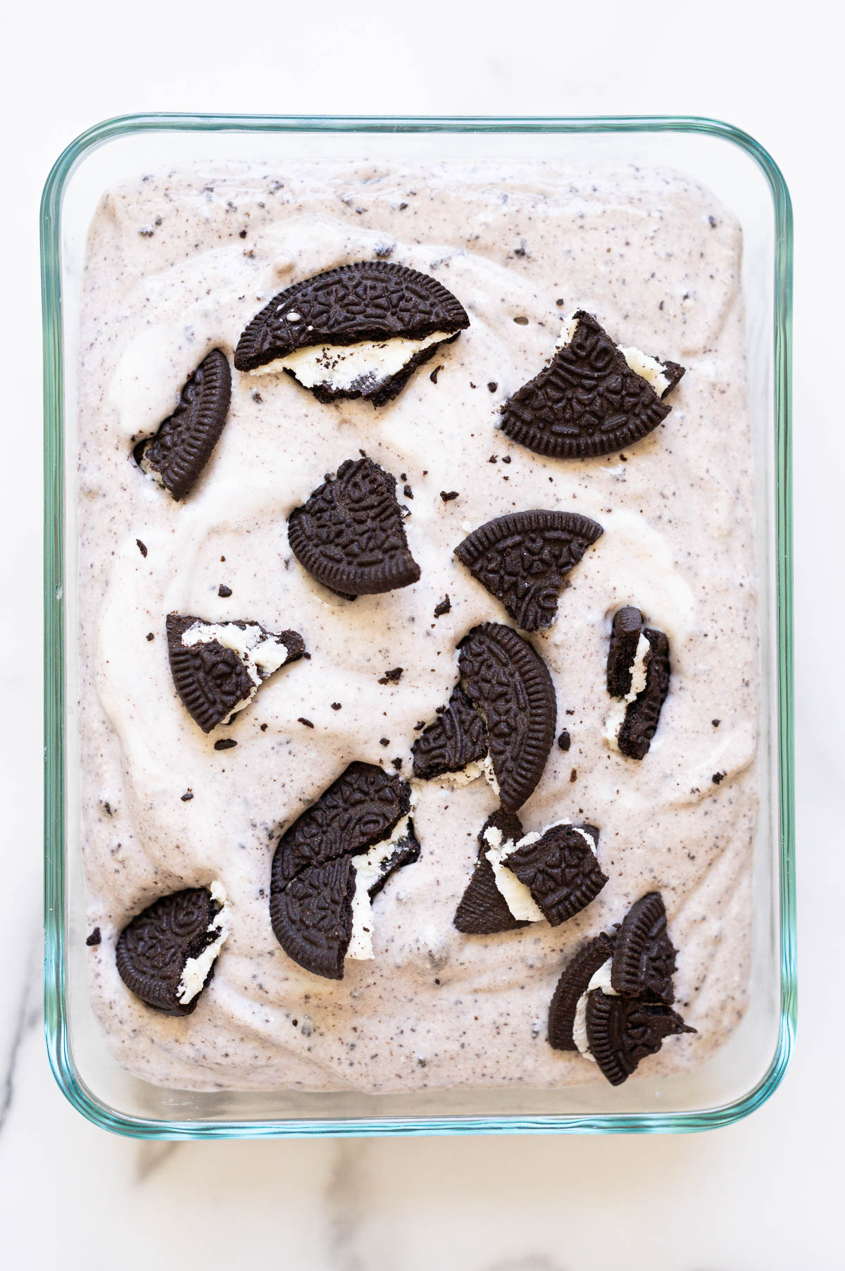 Cookies and cream cottage cheese ice cream topped with Oreo cookies in a glass container.