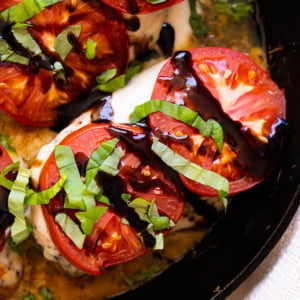 Baked chicken caprese garnished with balsamic glaze and fresh basil in a skillet.