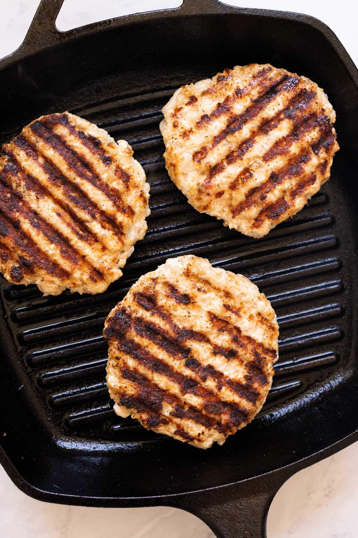 Three grilled chicken patties on cast iron grill pan.