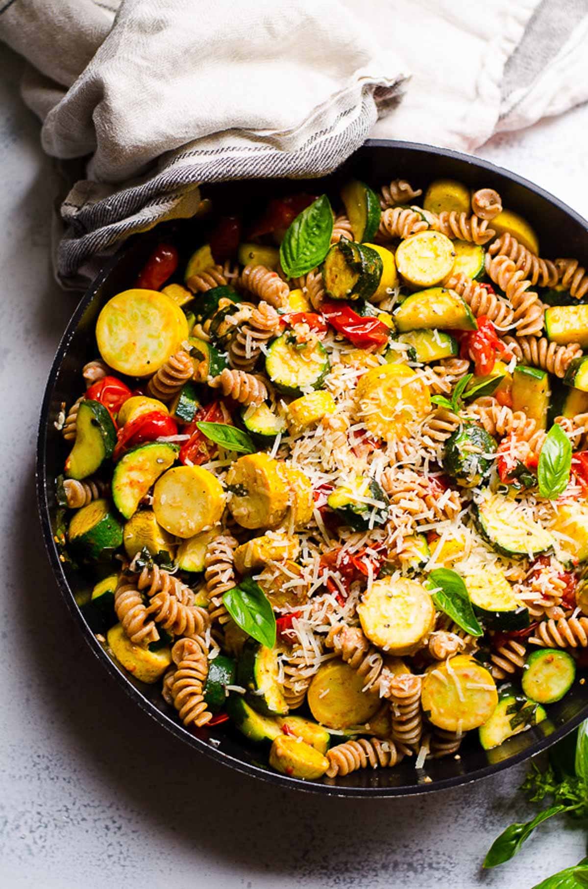 Pasta with zucchini and tomatoes garnish with Parmesan cheese in cast iron skillet.